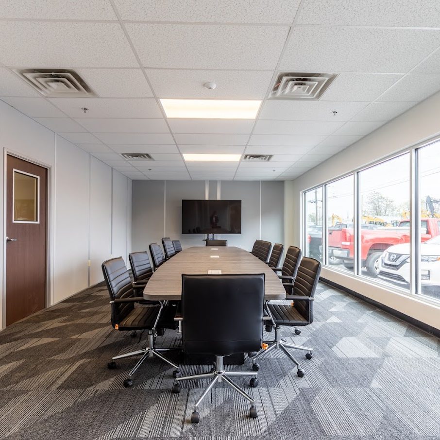 Modern conference room with a large table, chairs, and a window showing vehicles outside.